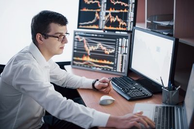 Stockbroker in shirt is working in a monitoring room with display screens. Stock Exchange Trading Forex Finance Graphic Concept. Businessmen trading stocks online.